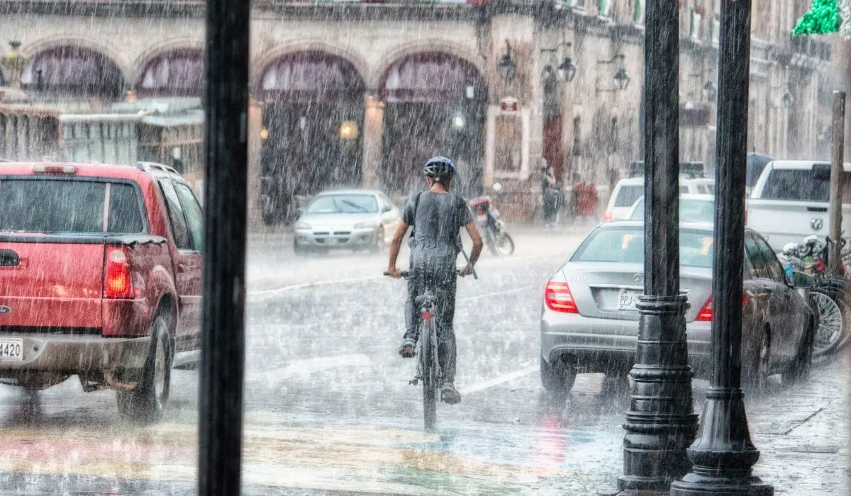 A person riding a bike in traffic in the pouring down rain. 