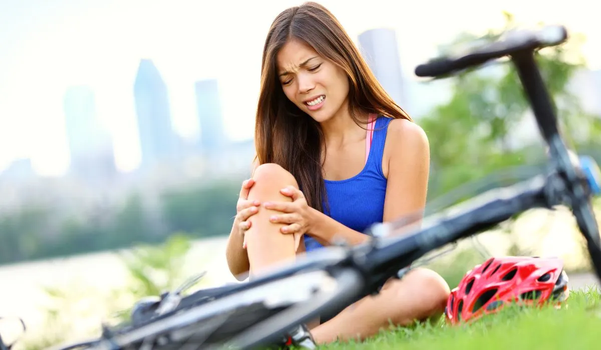 A cyclist sitting on the ground beside her bike holding a sore leg. 
