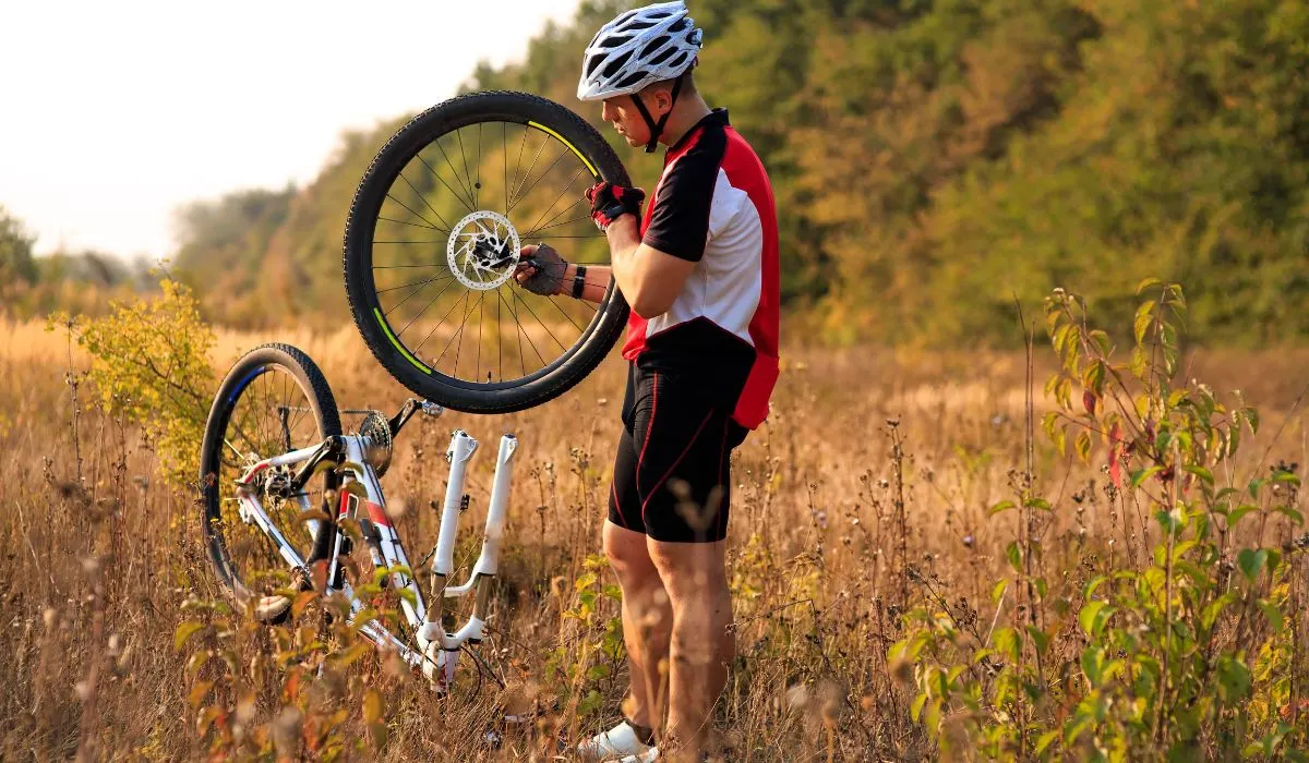 A cyclist stopped in a field holding one wheel of the bike, which is turned upside down. The person is repairing their bike. 