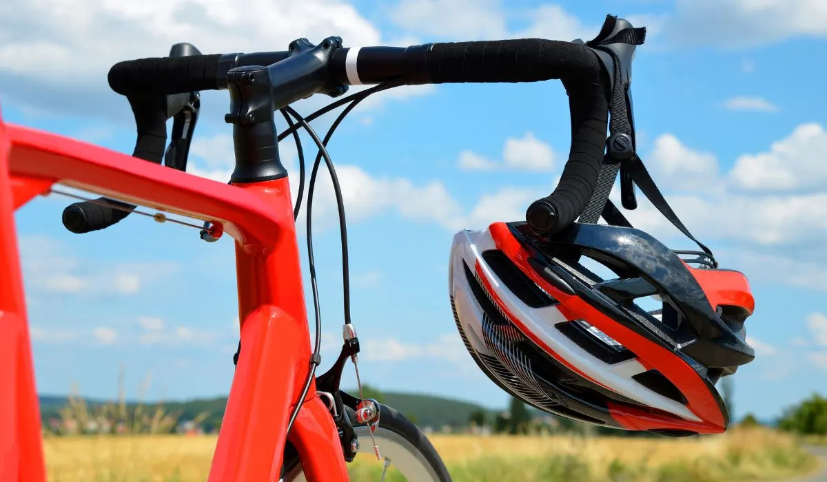A red bike with a black stem and handlebars with a helmet hanging off. 