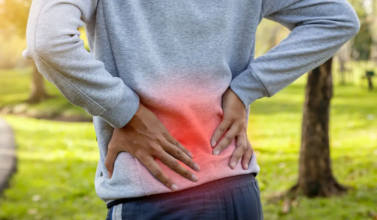 A person holding their lower back that is lit up red with pain. 