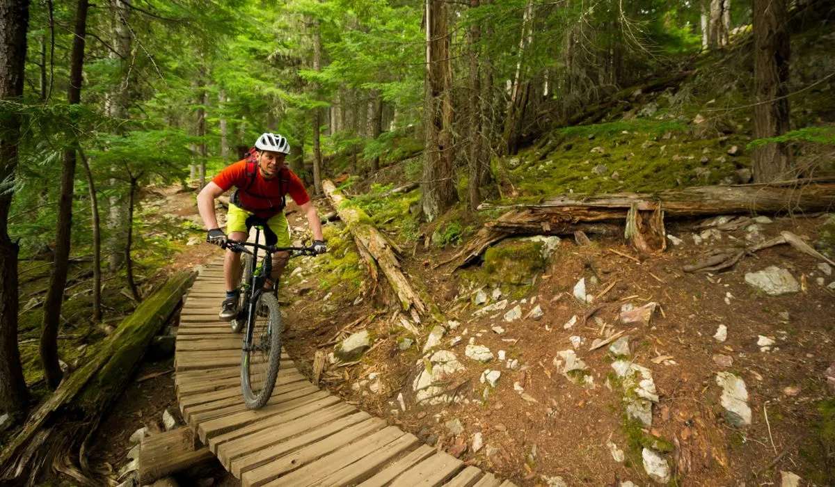 A man riding a bike over an uneven wood bridge. 