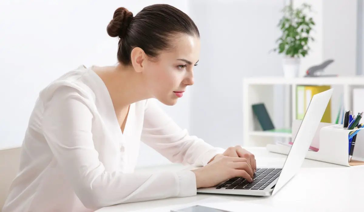 A woman sitting at a desk looking at t laptop with a slouched position. 