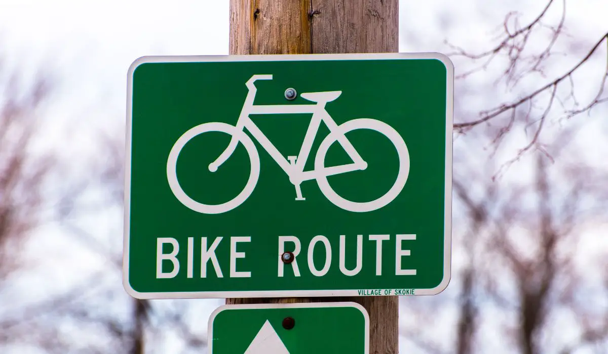 A green sign with white writing and a white bike that reads bike route. 