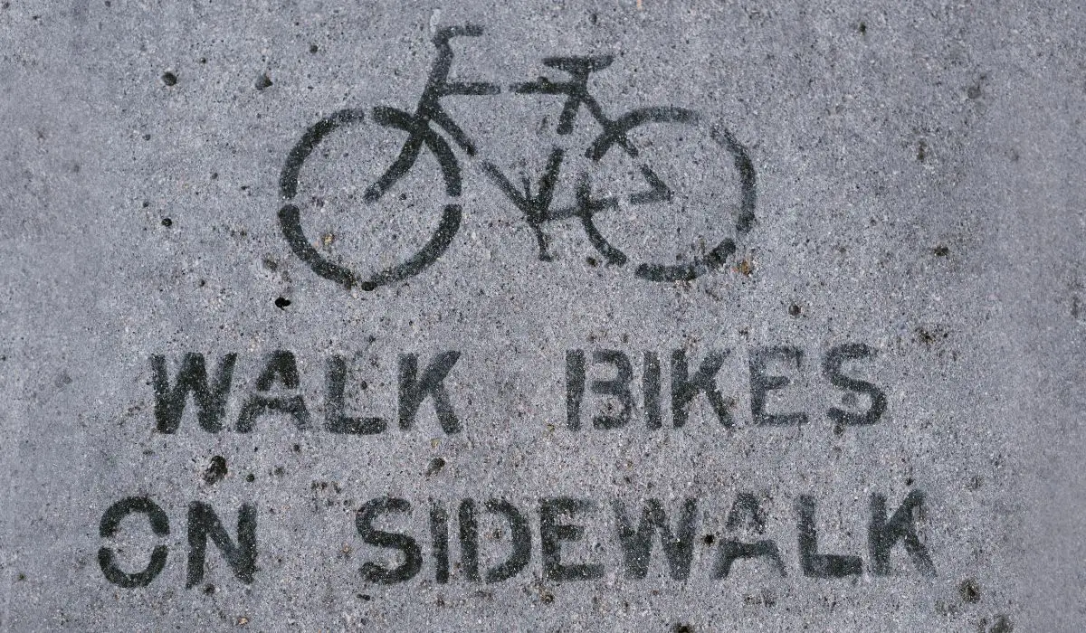 A painted notice on a sidewalk with a bike and words that read walk bikes on sidewalk.