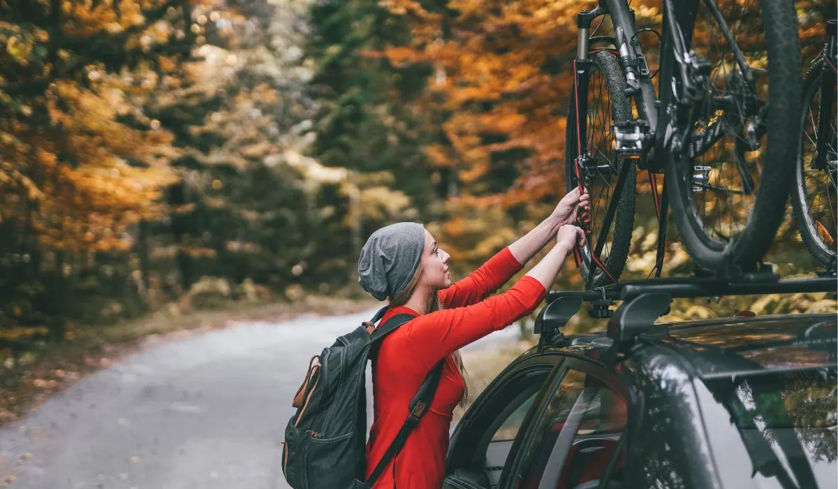 A person in a red shirt with a backpack securing a bike to a roof mount bike rack. 