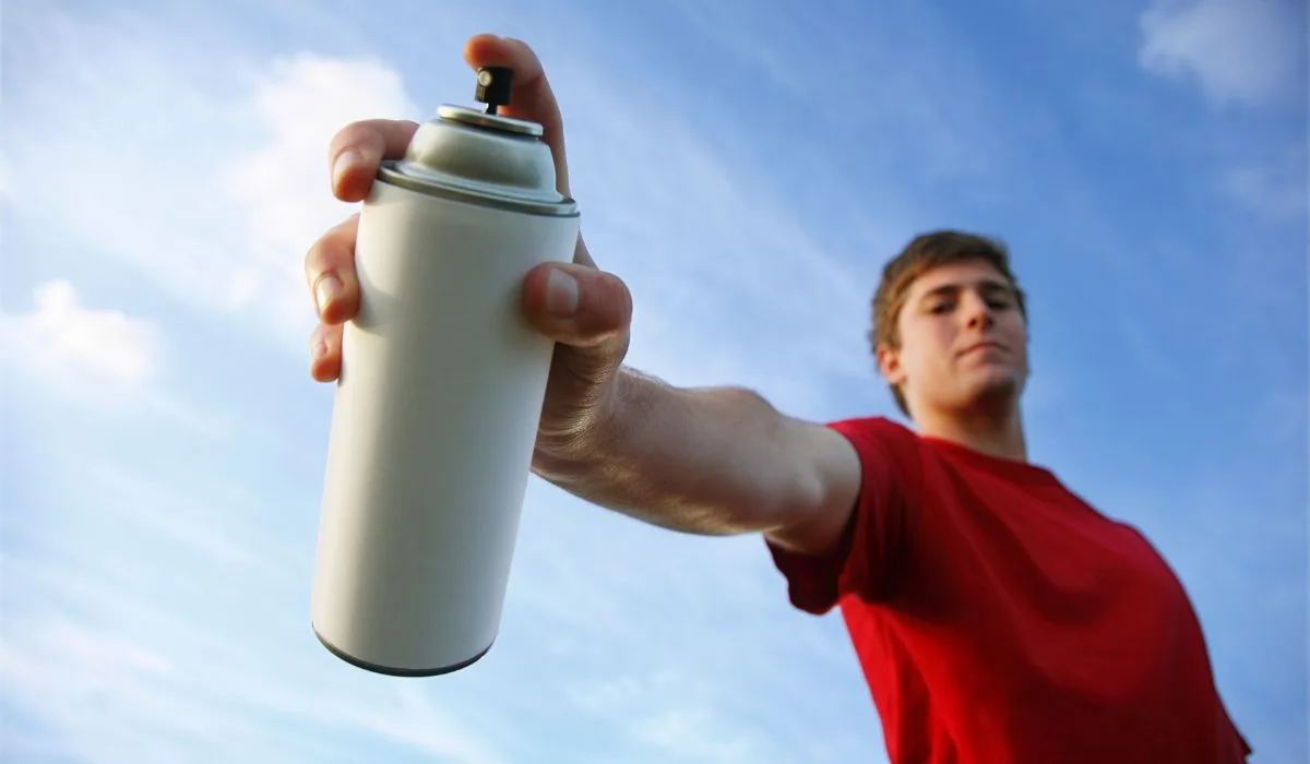 A person holding a spray paint can out to use, with a blue sky in the background.