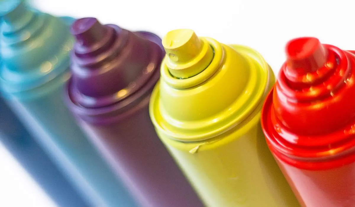 Solid color spray paints lined up with a white background, in blue, purple, yellow, red.