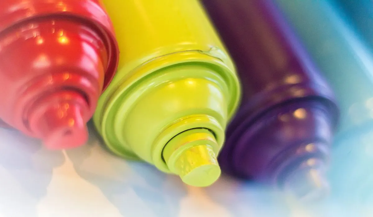 Cans of spray paint lined up laying on their side, in red, yellow, purple, blue.