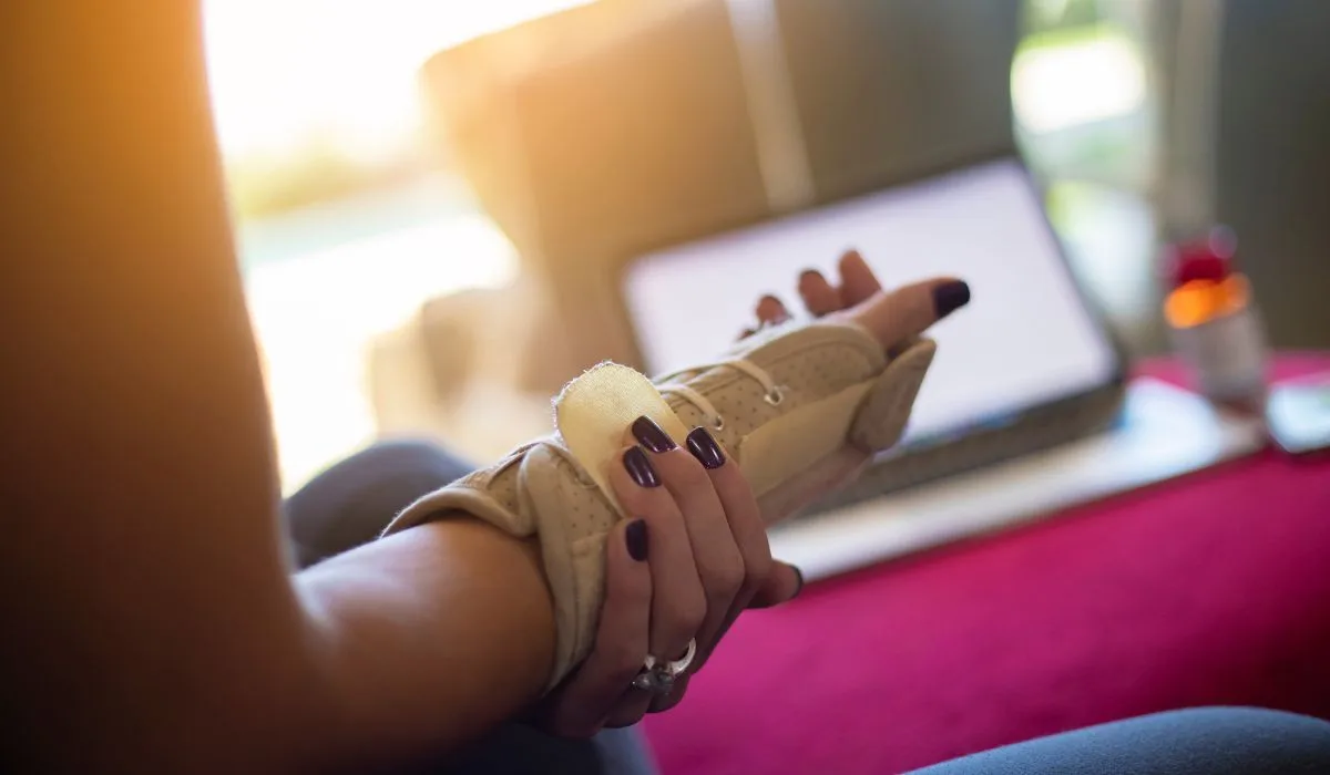 A woman with a wrist brace on and supporting her wrist with her other hand.