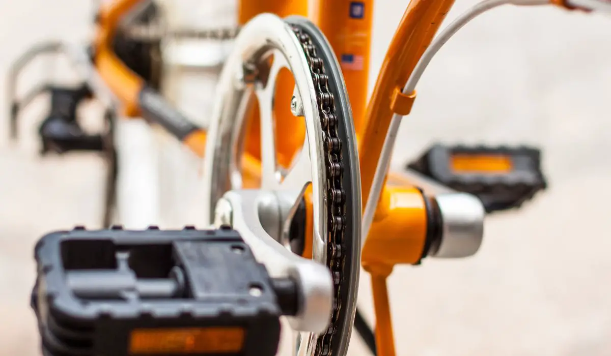 A close up of an orange bike pedals and gear. 