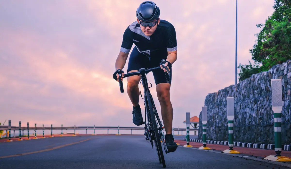 A front view of a cyclist on a road bike with sunset clouds behind them. 