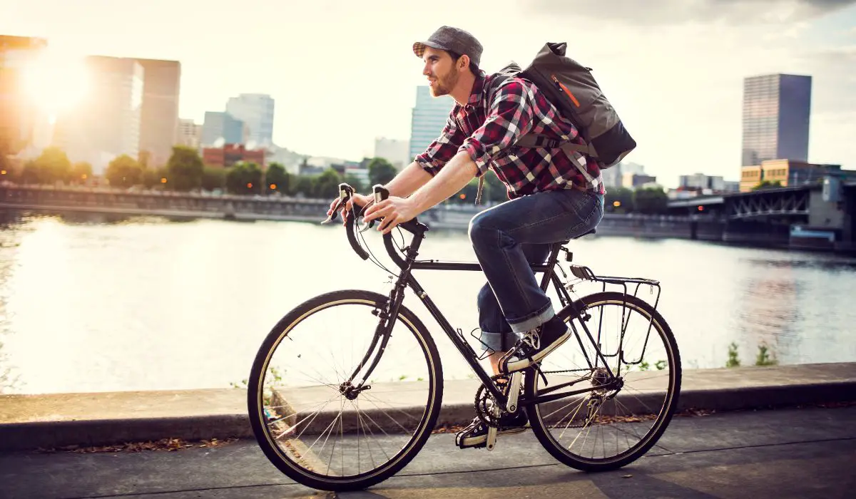 A man in jeans with a backpack cycling to commute to work. 