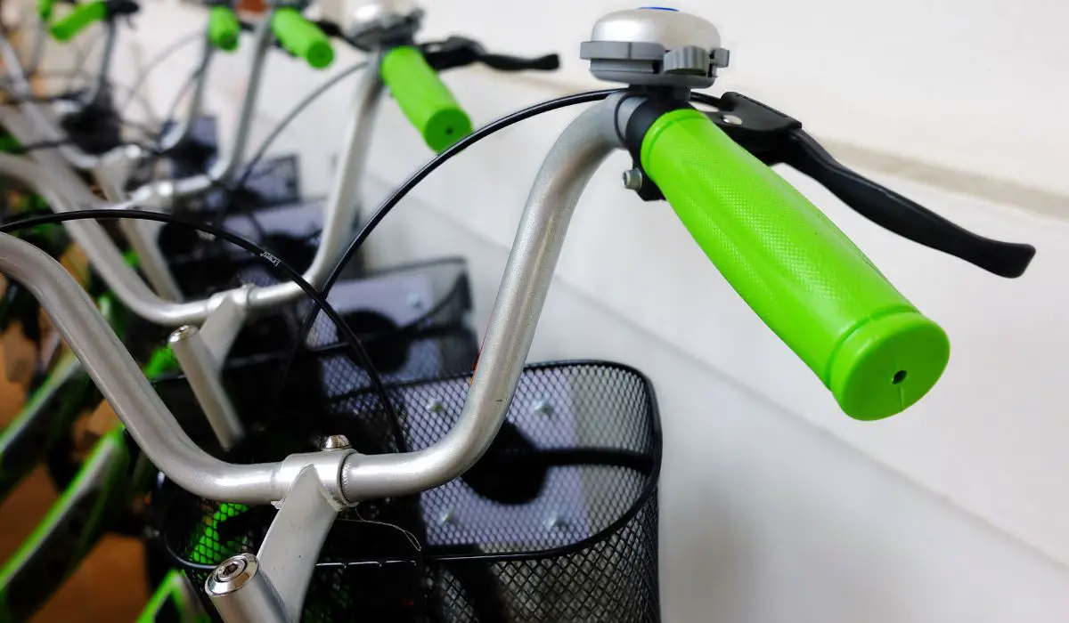 Bikes lined up with taller easy to reach handlebars that have green grips on them. 