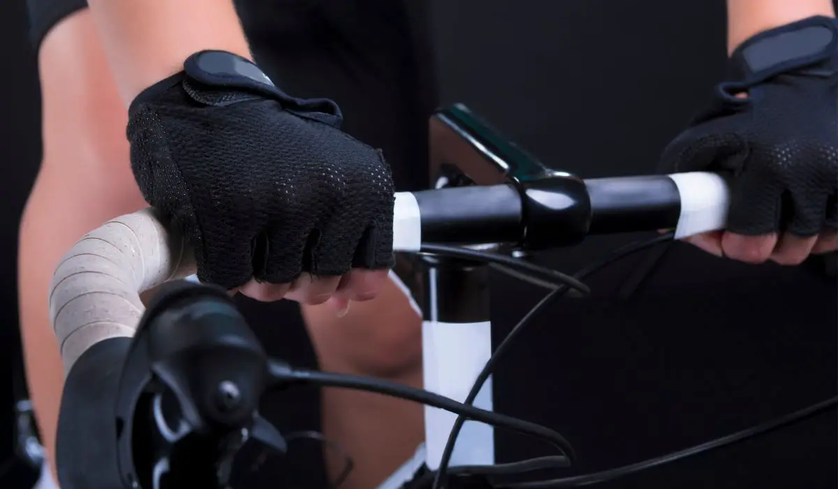 A cyclists hands holding onto handlebars with fingerless gloves for cycling on. 
