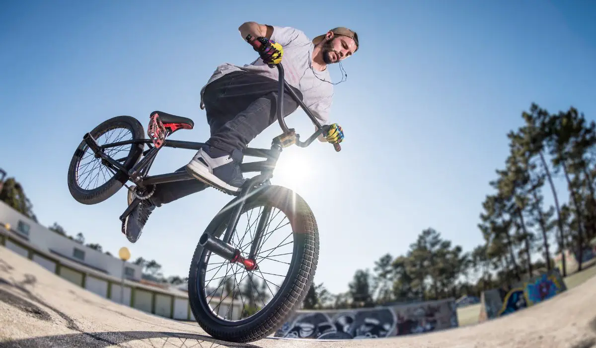 A man doing a stunt on the front wheel of a 24" bike on a ramp, with the sun shining behind.