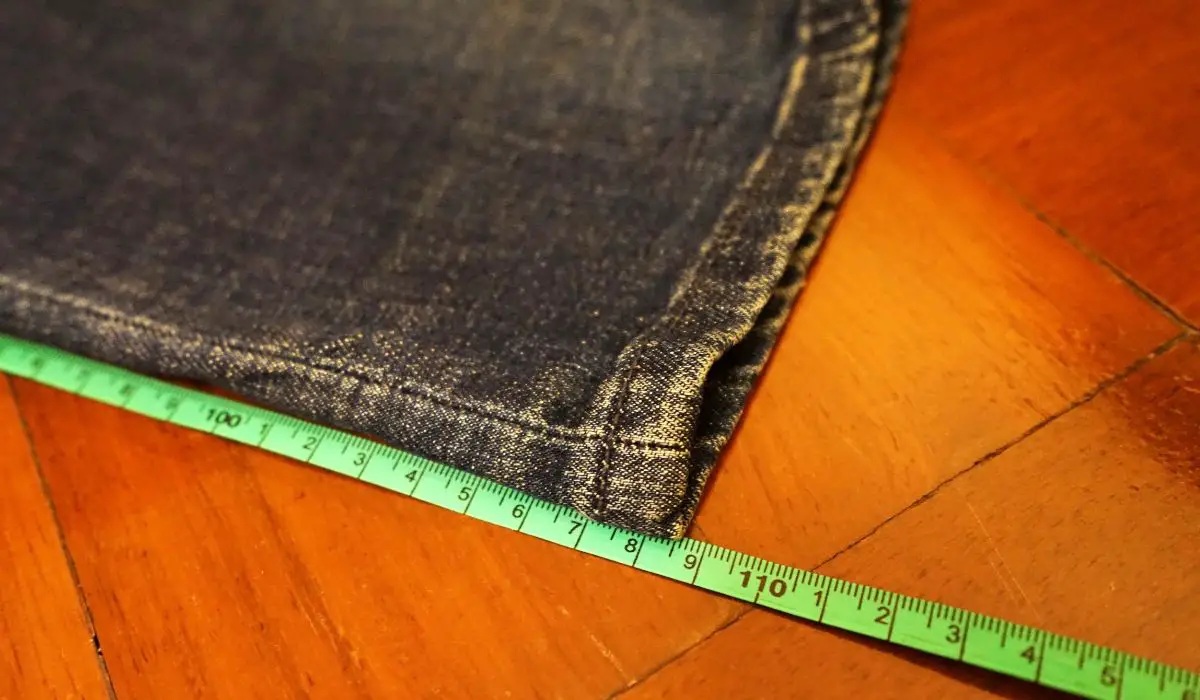 A pant leg on a table with a measuring tape measuring the length. 