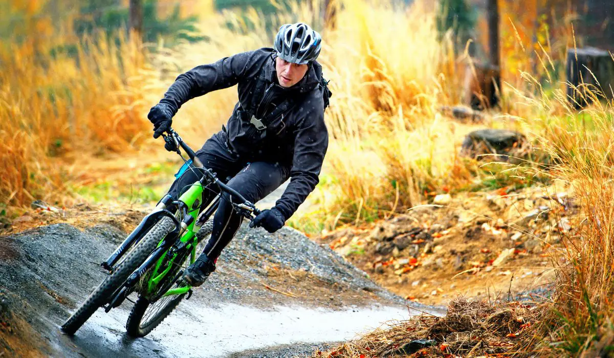 A man riding a mountain bike on a steep trail with fall colors in the background, and him appearing to be very far leaned over to one side. 