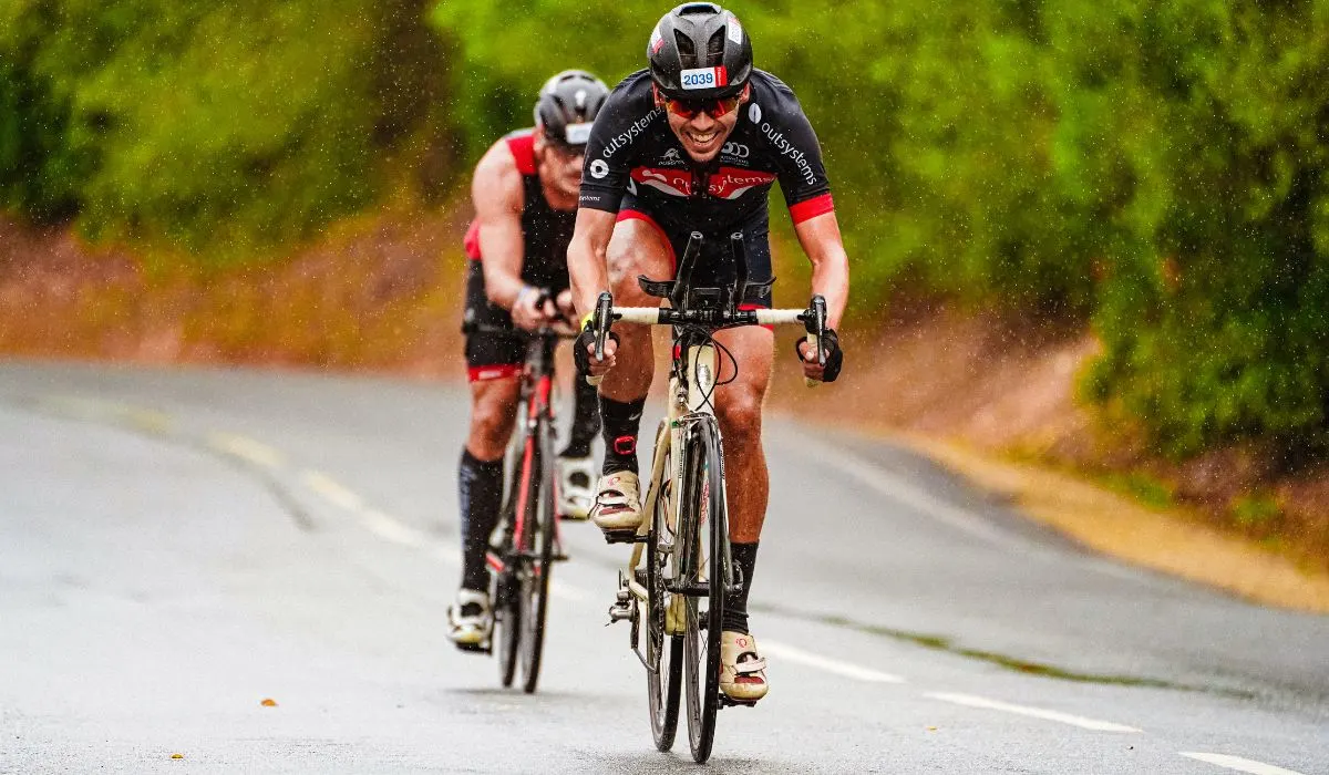 2 men on road bikes on a forested road.