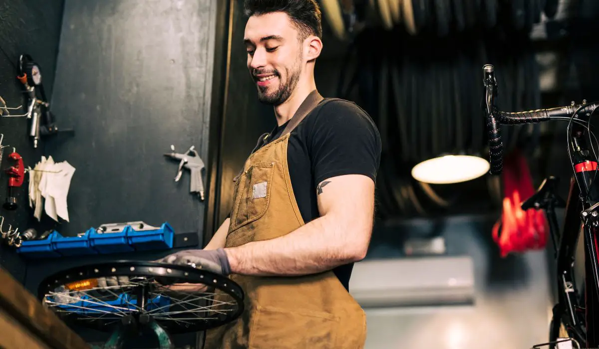 A man in a work vest in a shop servicing a bike. 