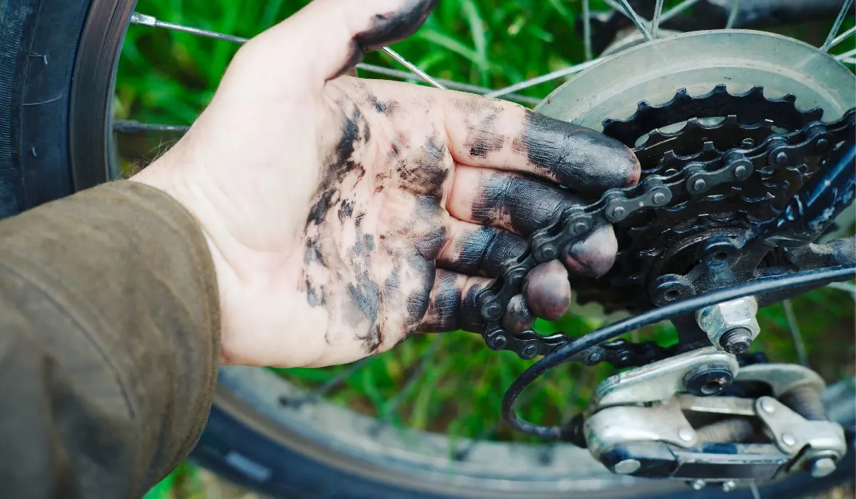 A hand with black grease on it holding a bike chain that is still attached to the bike.