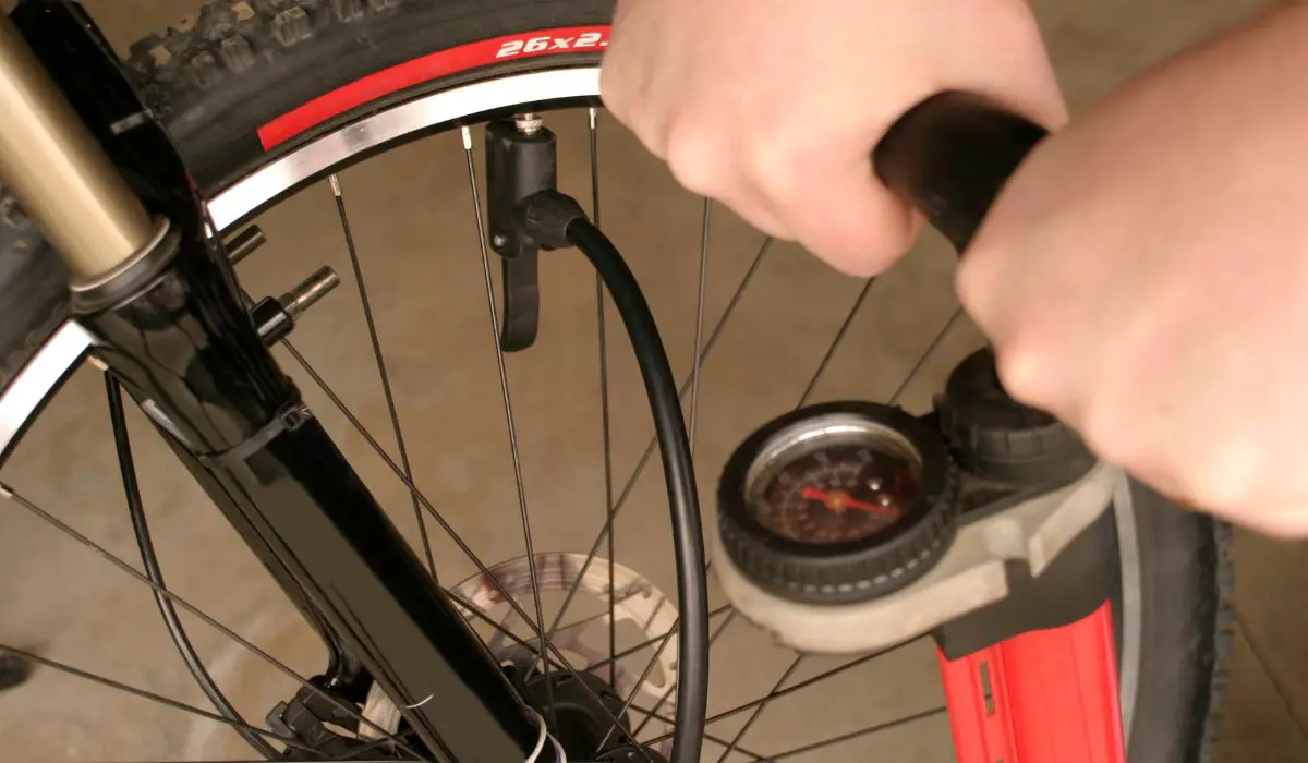 A close up photo of a bike tire with hands pumping an air pump with a pressure gauge on it.