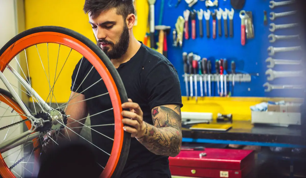 A man with a bike upside down working on the wheel with an orange painted rim. 