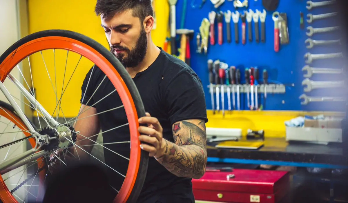 A man with a bike upside down working on the wheel with an orange painted rim.