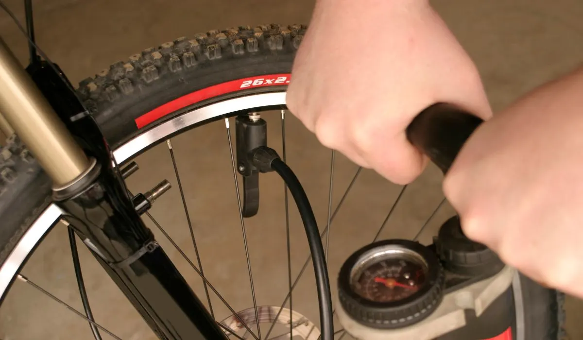 A bike pump on a bike tire with hands pumping it.