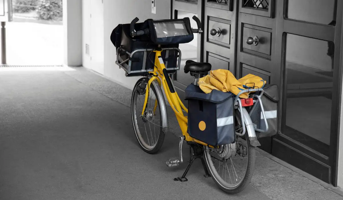 A bike parked that has bags on each side, and is also holding a box in front of the handlebars. 