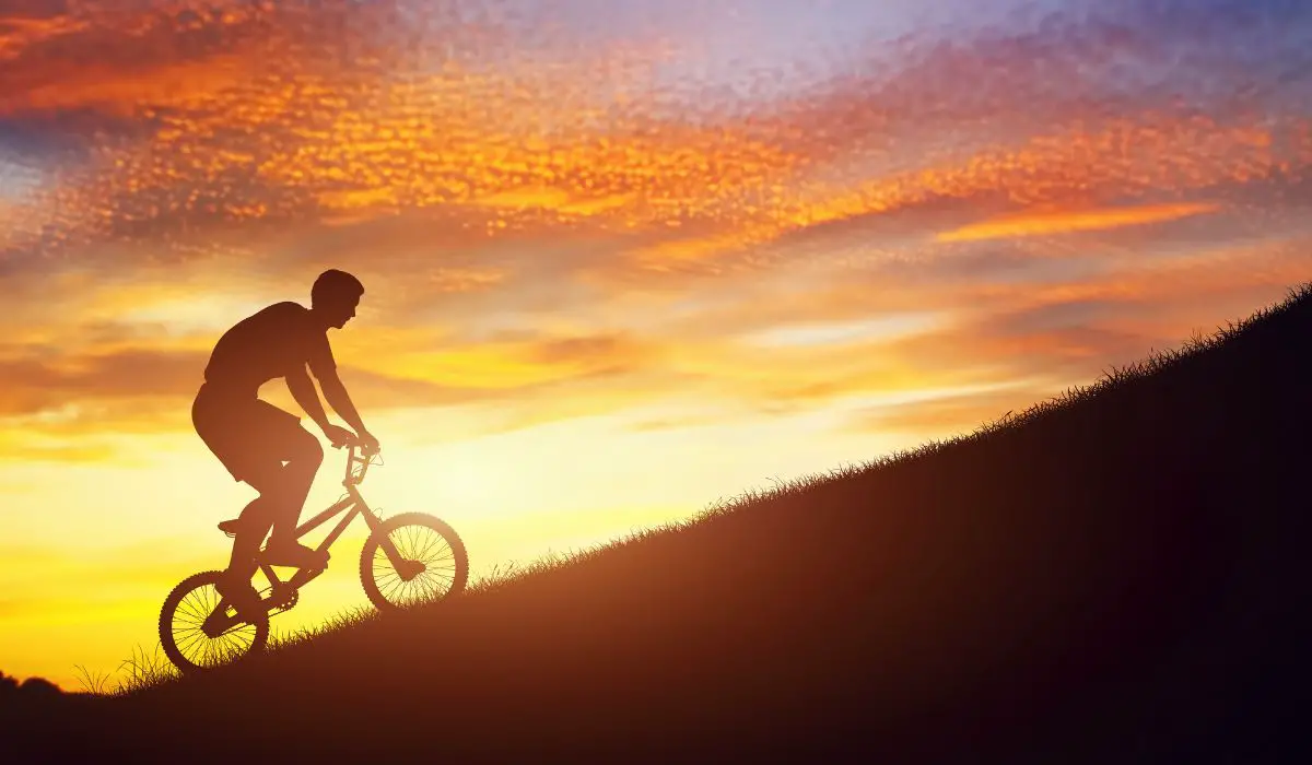 A sunset background showing a figure riding a bike up a steep hill.