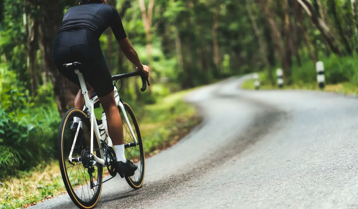 A road cyclist riding up a hill on a forested street. 