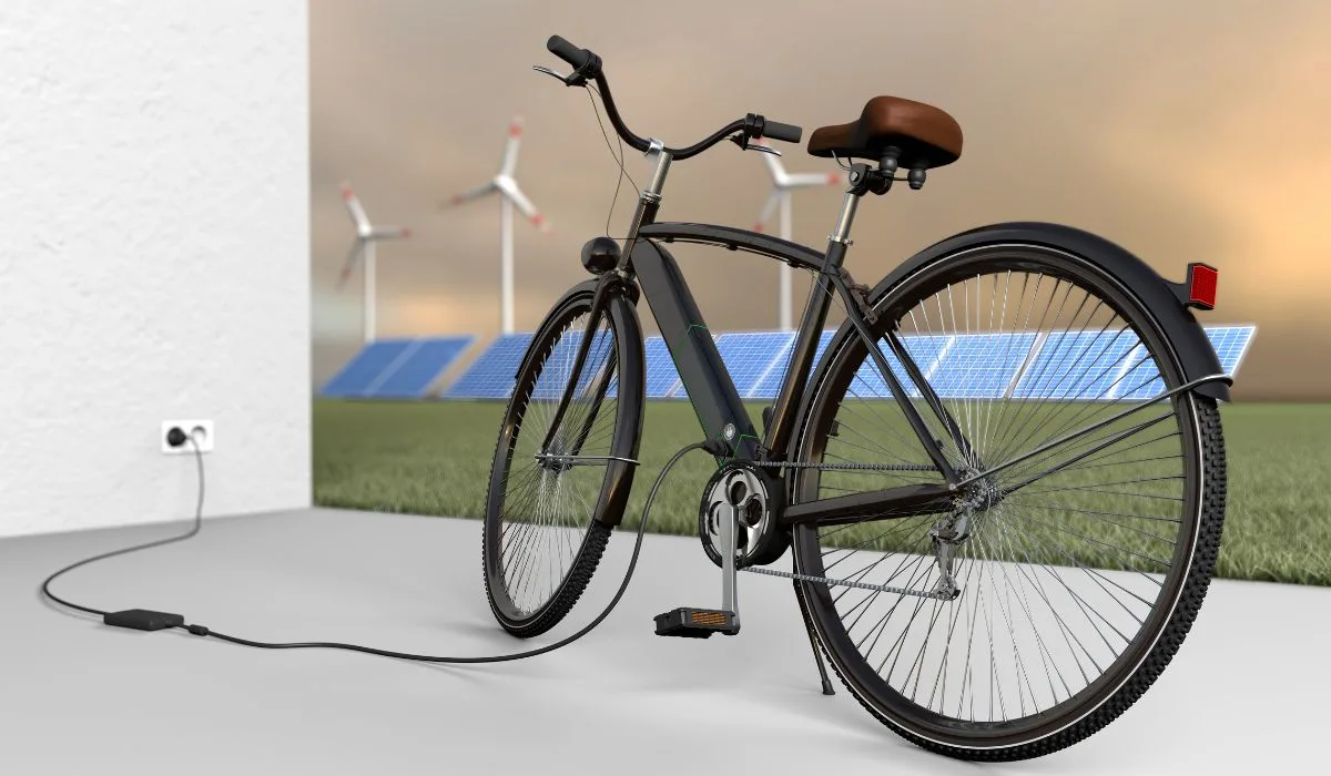 An electric bike plugged into a wall outlet with a display of solar panels and energy windmills in the background.