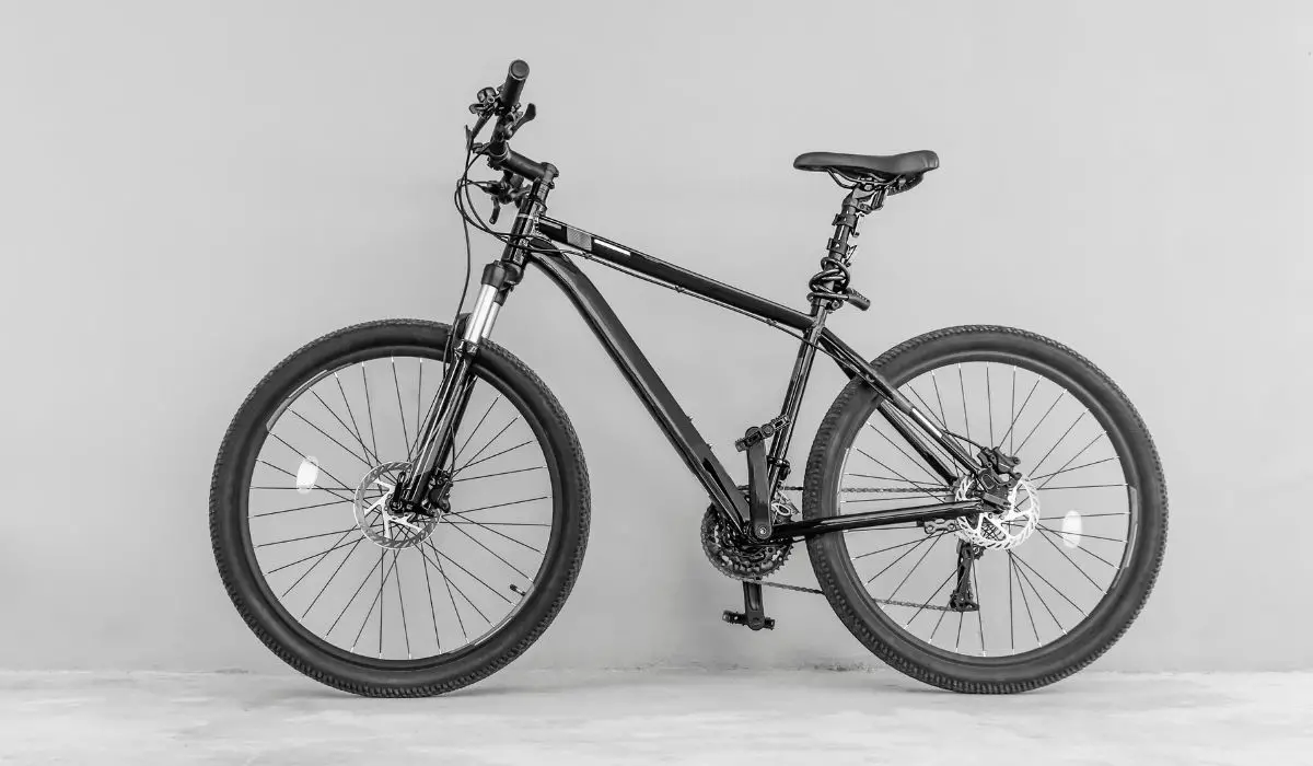 A black mountain bike leaning up against a light gray wall. 
