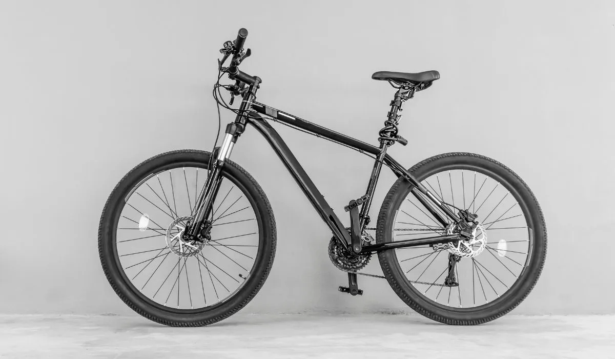 A black mountain bike leaning up against a light gray wall. 