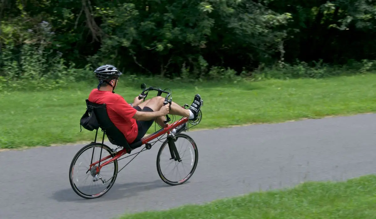 A person riding a recumbent bike on a path with grass on each side. 