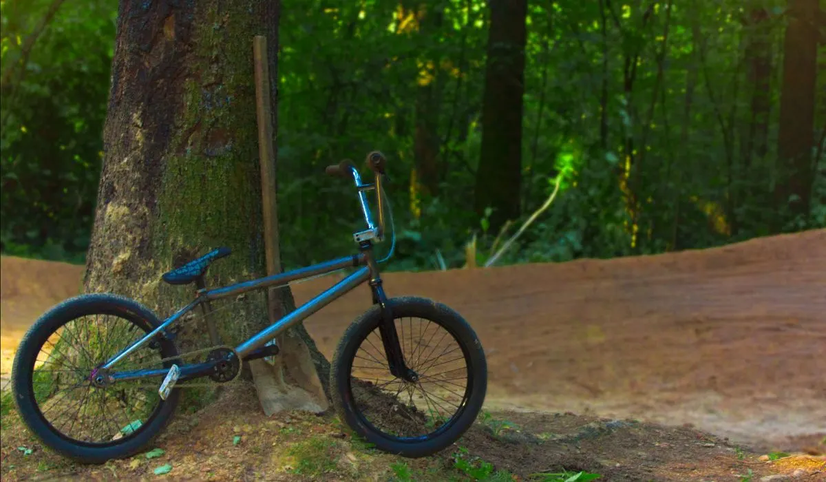 A blue bmx bike in a forest leaning up against a tree. 