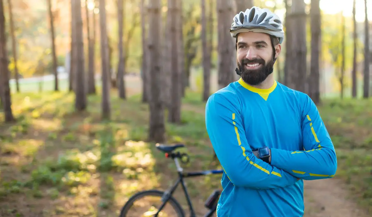 A man with a big smile in the woods with his mountain bike behind him.