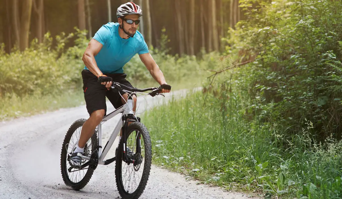 A man riding a mountain bike on a gravel path through the woods.