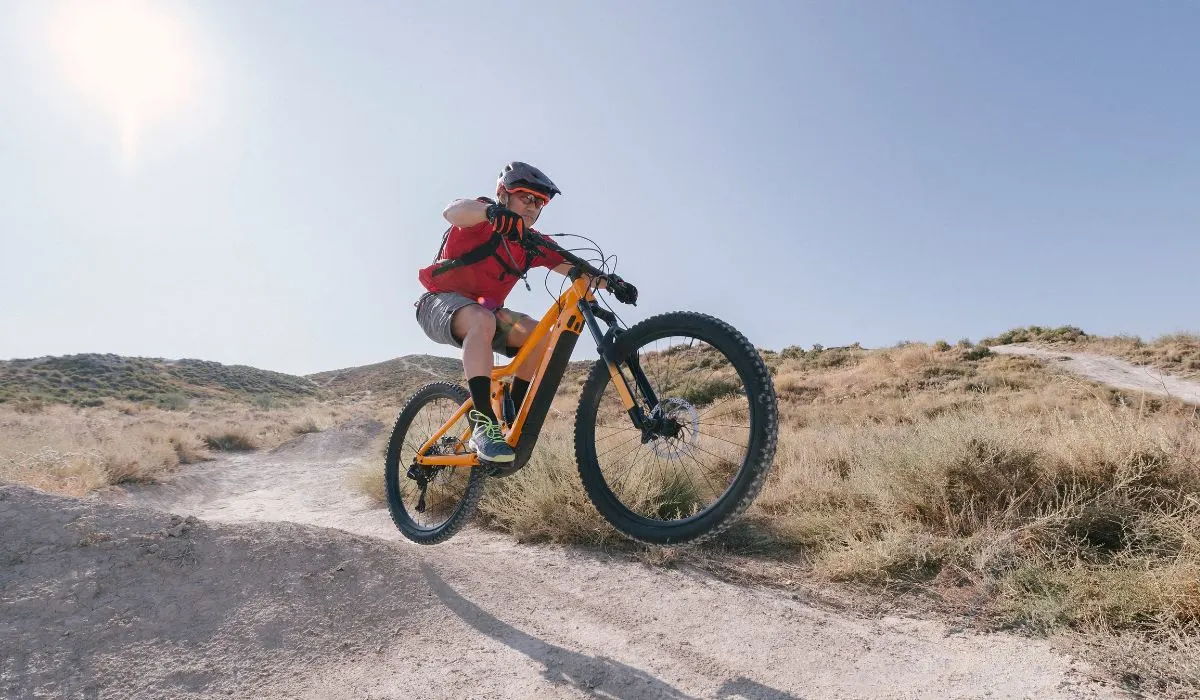 A man on an electric bike jumping a small hill on a dirt path. 