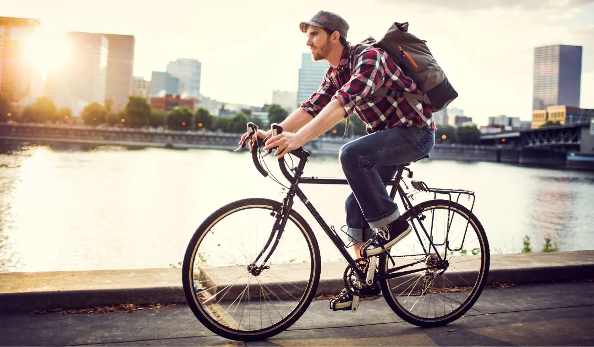 A man commuting on a retro looking bike with a backpack, next to a river.
