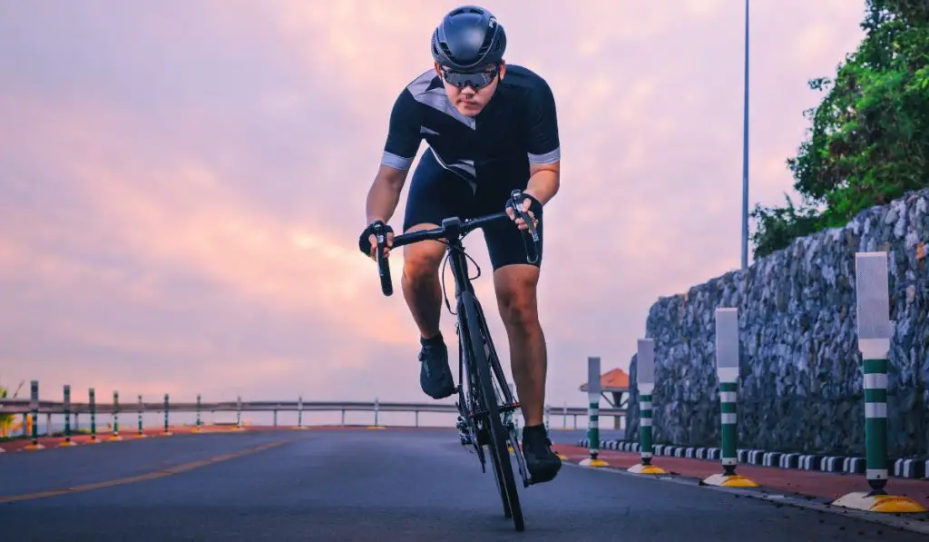 Front view of a man on a road bike with a purple and pink sunset in the background. 