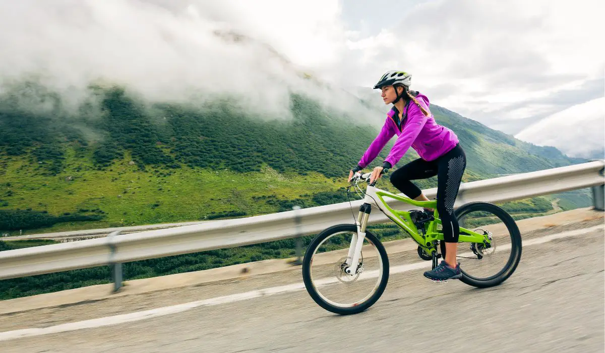 A woman on a bike riding on a road in the mountains. 