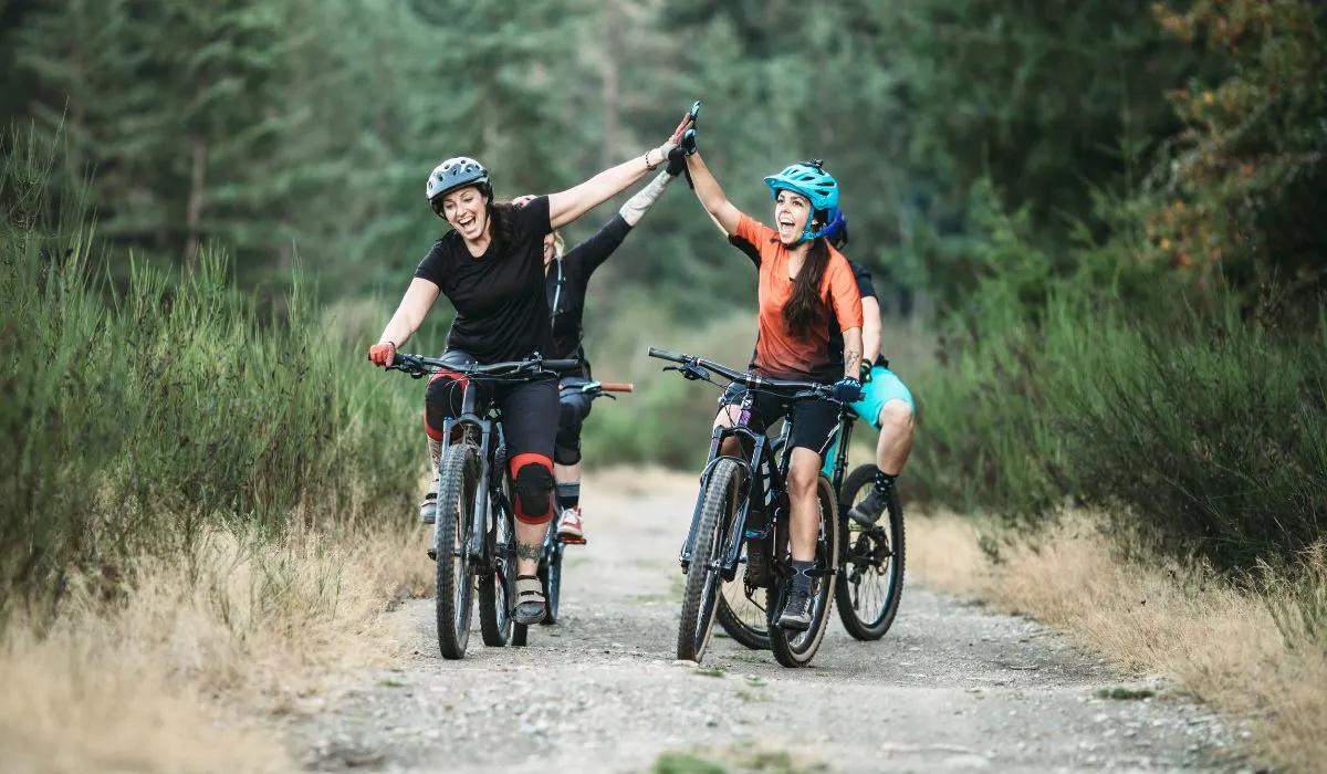 A group of women on mountain bikes on a gravel trail. Two women in front giving high fives.