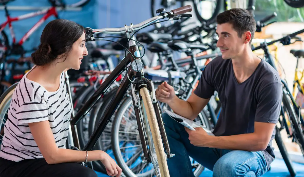 A man and woman at a bike shop crouched down looking at a bike to buy, with more bikes for sale in the background.