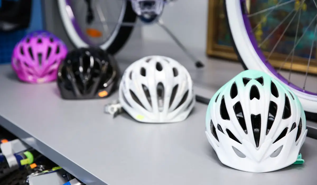 Bike helmets on a store shelf with bike wheels in the background. 