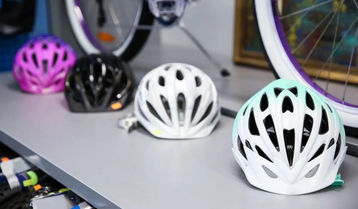 Bike helmets on a store shelf with bike wheels in the background. 