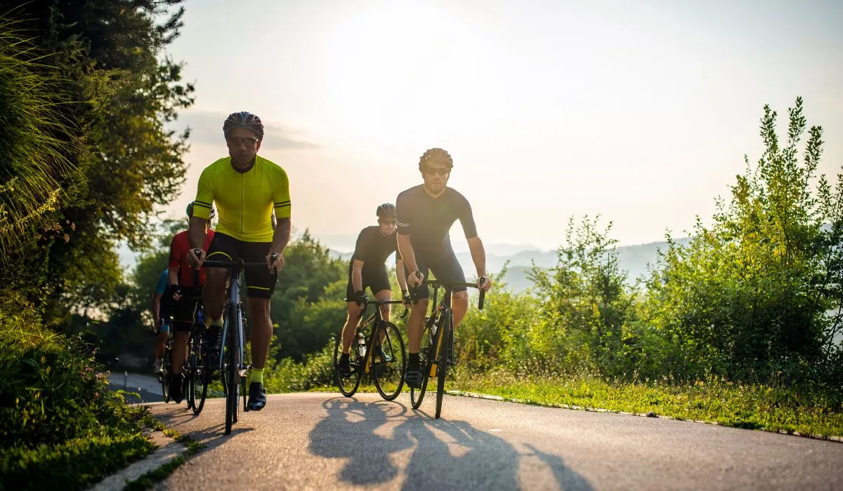 A group of people riding their bikes on a road with natural surroundings. 