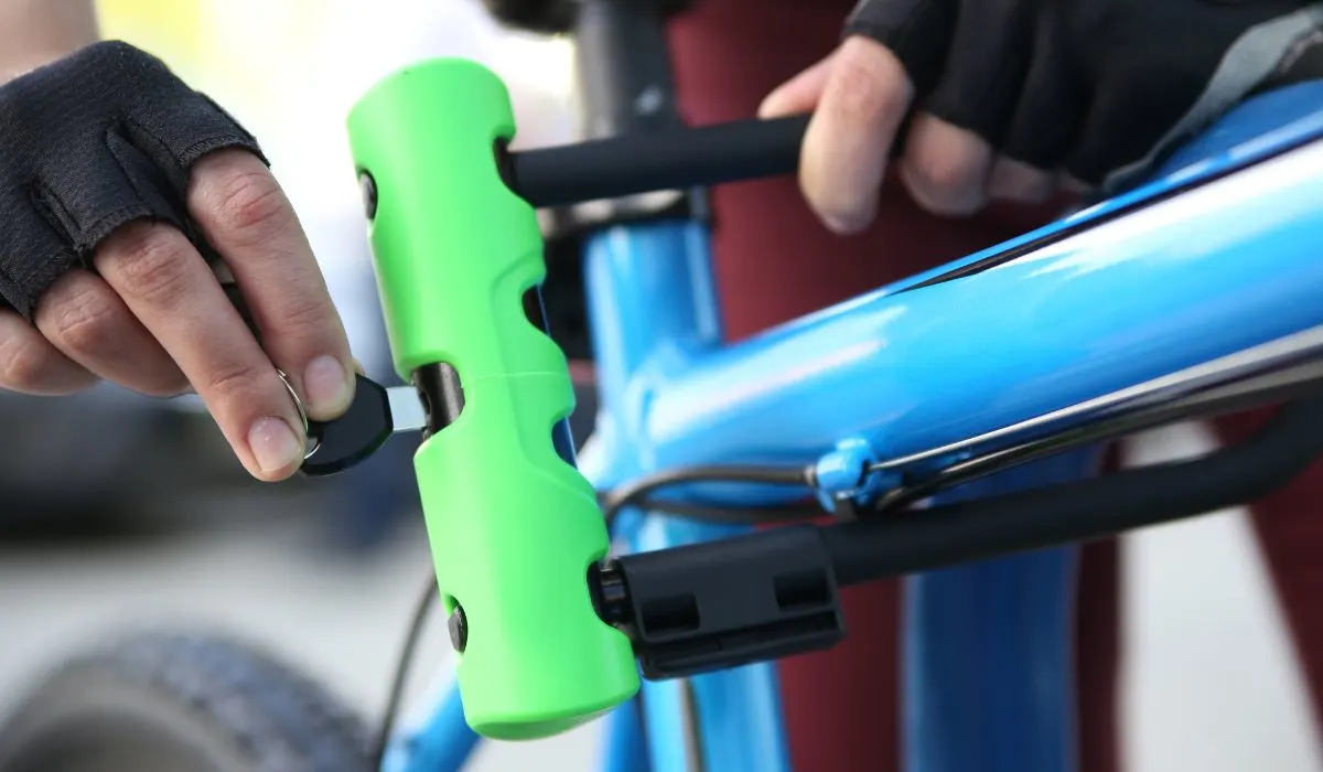 A hand locking a bike u lock with a key onto a bike frame. 