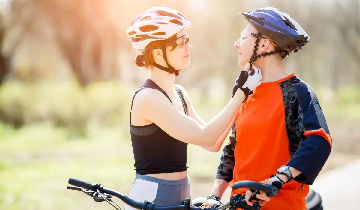 A woman strapping a helmet to a young man's head. 